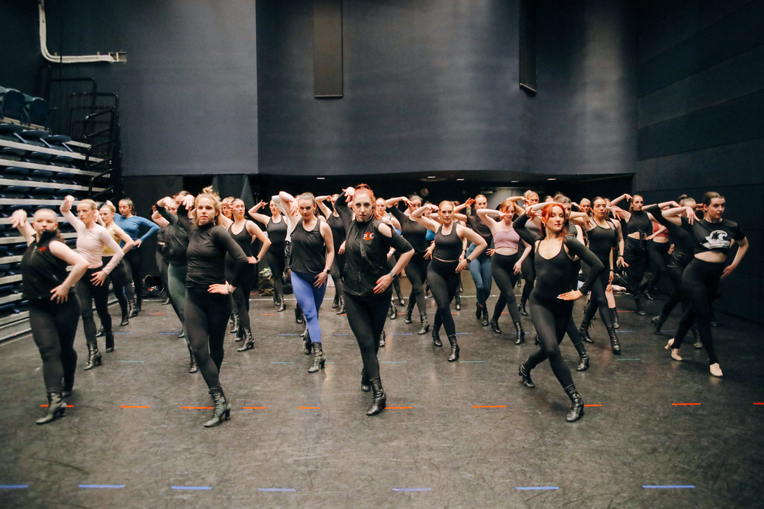 Large group of dancers rehearsing in unison with arms raised