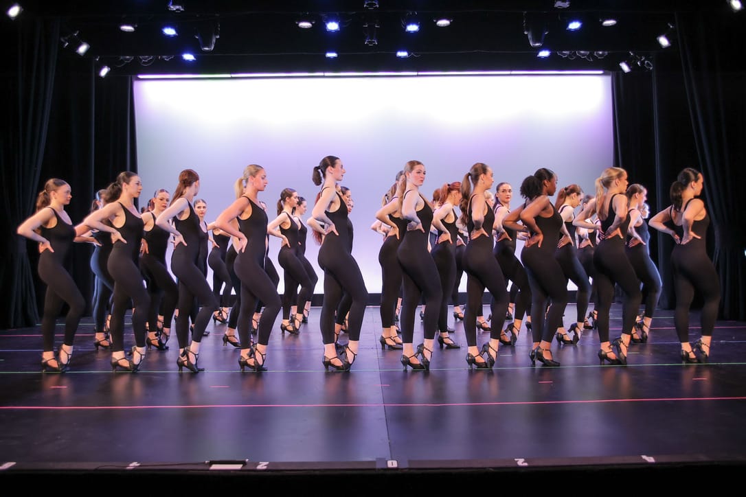 Long line of dancers performing on stage in matching black attire