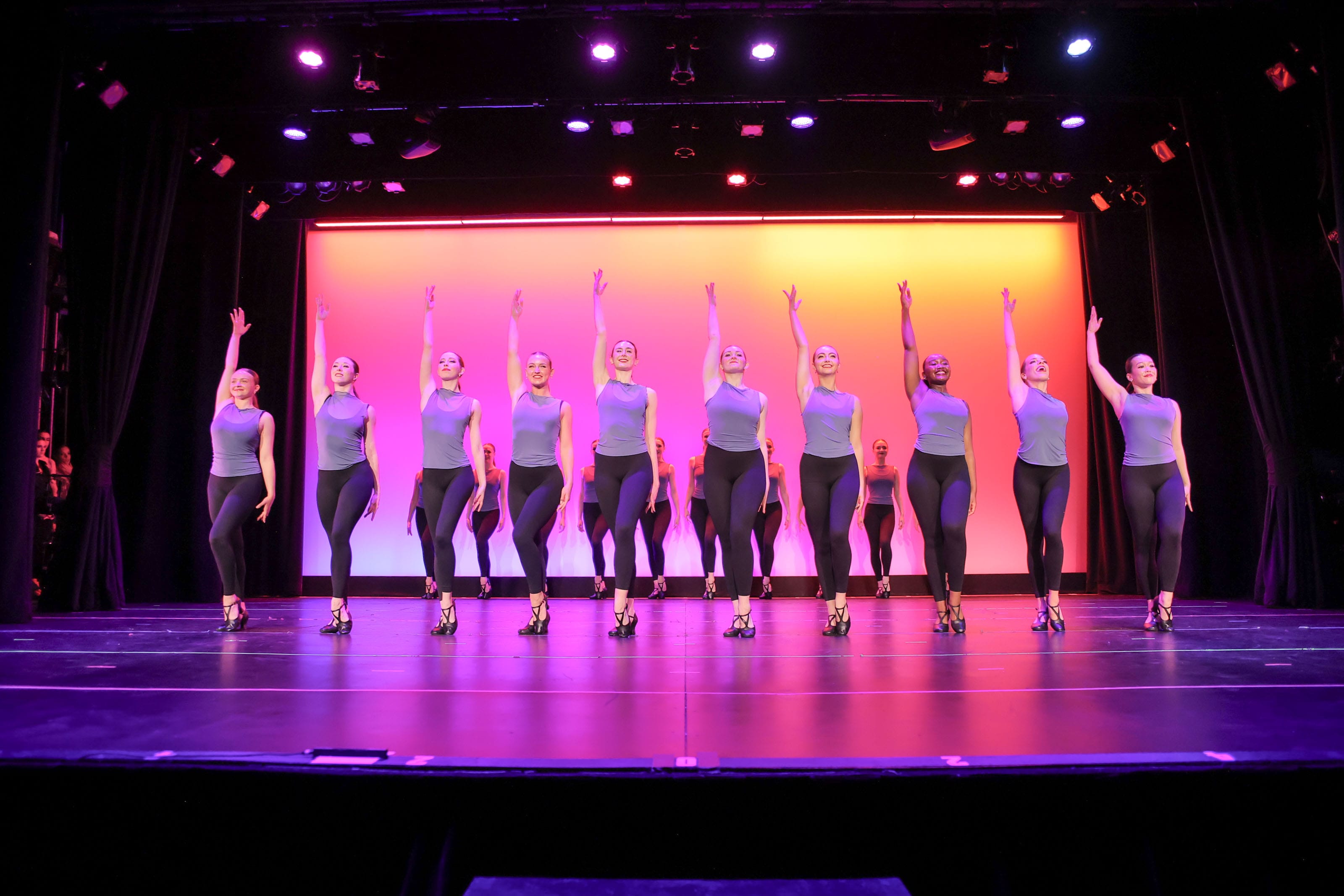 PDC dancers on stage in unison with arms raised during the Performance Collective live performance